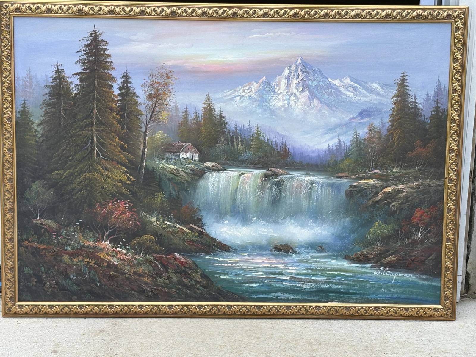 Framed oil painting of a snowy mountain, pine forest and waterfall in a gilt frame